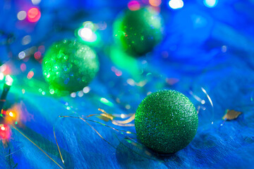 Closeup of the green glittering Christmas ball with another two decorations on the bright blue background. New year, winter holidays cozy atmosphere	