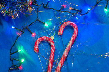 Top view of two Christmas candies with the colorful garland on the bright blue paper. New year, winter joy concept background