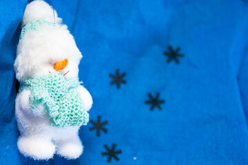 Closeup of a soft toy in a form of a snowman on the blue backround with silver snowflakes. Top view. New Year, Christmas background with the free space for text