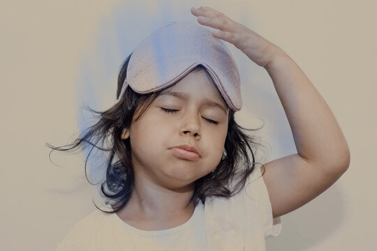 Tired sleepy little girl with sleep mask on her head, eyes closed, parasomnia
