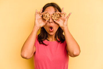 Young hispanic woman holding cookies isolated on yellow background
