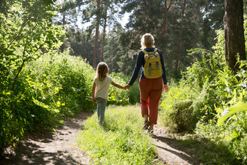 mom and and child daughter with backpack walking in the forest. Staycations, hyper-local travel,...