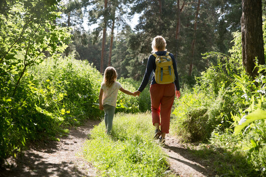 mom and and child daughter with backpack walking in the forest. Staycations, hyper-local travel, family outing, getaway, natural environ. Concept of friendly family. Family spends summer time together