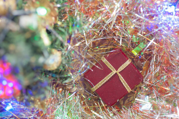 Maroon gift box with golden ribbon and colorful garland on a golden tinsel background. Top view. Christmas atmosphere, New year mood, winter holidays