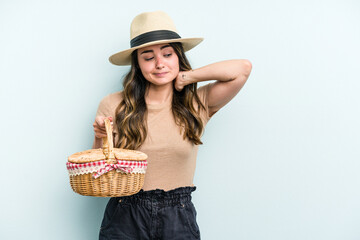 Young caucasian woman holding a picnic basket isolated on blue background touching back of head, thinking and making a choice.