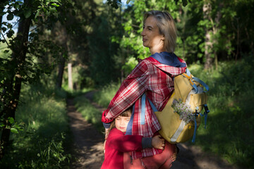 Obraz na płótnie Canvas mom and and child daughter with backpack walking in the forest. Staycations, hyper-local travel, family outing, getaway, natural environ. Concept of friendly family. Family spends summer time together