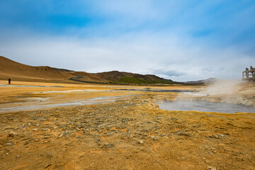 People observe grounds of Hverir geothermal area in the north of Iceland. Steam coming out of hot mud pots emitting sulfur gases.