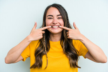 Young caucasian woman isolated on blue background smiles, pointing fingers at mouth.