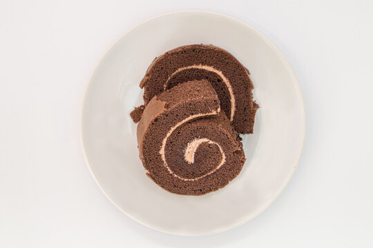 Peeling Off Jam Rolls On The White Plate Isolated On White Background. A Close-up Coffee Roll Cake. Cappuccino Roll Cake. Swiss Roll Cake. Imperfect Jam Rolls.