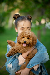 A cute teen girl on a walk with toy poodle dog. It's spring outside. The girl is dressed in a blue jacket in a flower and jeans. Childhood. Pets.