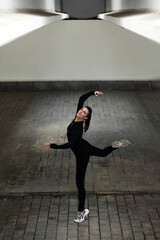 Portrait of young dance girl in black standing in elegant pose during dancing on the street