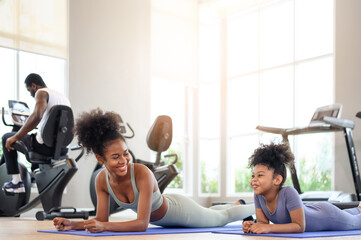 African American mother and daughter in sportswear practicing yoga together on yoga mat at the gym. Black family sporty fitness workout.