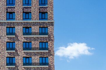 Fototapeta premium multi-storey brick residential building against a blue sky with clouds. Text space, template for advertising, booklet. The concept of construction, mortgages, home insurance, housewarming