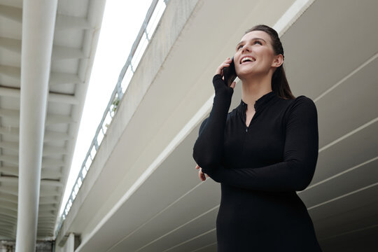 Young female dancer in black sportswear talking on mobile phone and laughing after training on the street