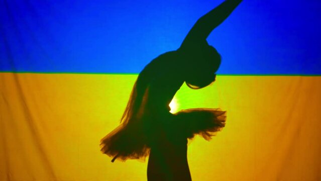 Side view silhouette of ballerina at Ukrainian flag with backlit raising hands praying. Graceful skilled dancer performing at background of national flag. Hope concept