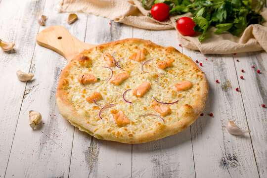 Pizza with salmon and red onion with cheese on white wooden table