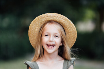 Candid lifestyle portrait of cute little caucasian girl with blonde hair and smiley face wearing straw hat outdoor at hot summer day.