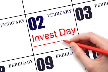 Hand drawing red line and writing the text Invest Day on calendar date February 2. Business and financial concept.