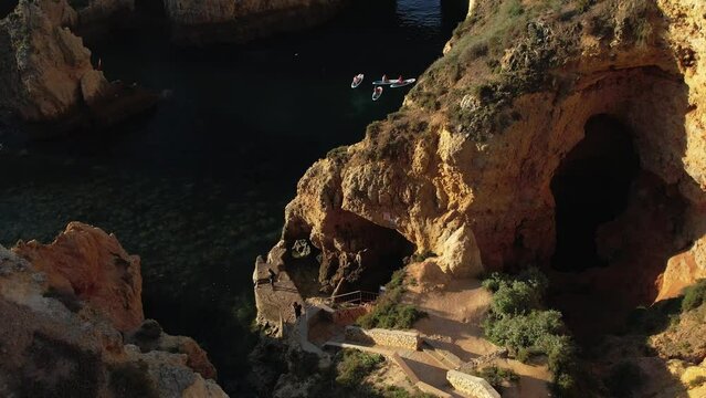 SUP Tour in a small rocky cove. Slow reveal by drone. Stand Up Paddle Boarding on a sunny morning, in between caves and cliffs in South Portugal.