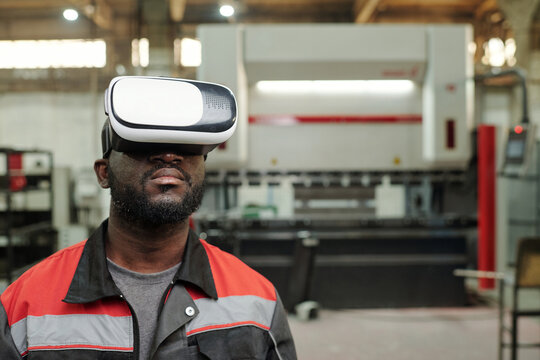 Young serious African American male engineer in vr headset making presentation of industrial equipment while standing in workshop