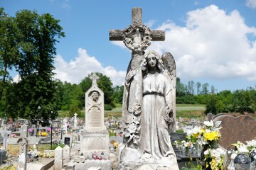 Fototapeta na wymiar Figure of angel with cross at cemetery in Pelczyska, Ponidzie, Swietokrzyskie, Poland. The sculpture is made of Pinczow limestone (pinczak).
