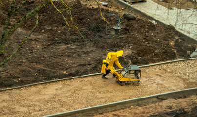 a worker in a yellow raincoat rams the sand - obrazy, fototapety, plakaty