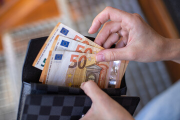 A woman's hands take euro banknotes out of her wallet