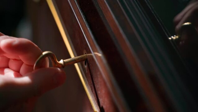 Turning a golden key in the keyhole of an old wooden sideboard and opening a secret door