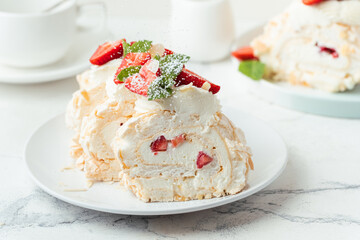 Meringue roll sprinkled with powdered sugar decorated with strawberries sliced and served in the white plate on the white background. Macro shot