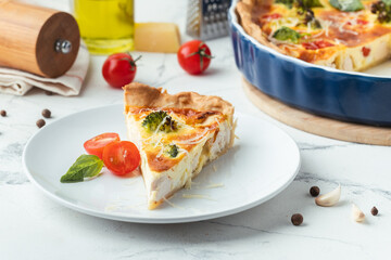 Quiche with chicken decorated with tomatoes, basil and broccoli. French pie with shortcrust pastry base on the white marble background
