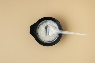 Flat lay of hairdresser equipment for mixing hair dye. Professional black jar with a brush on beige...