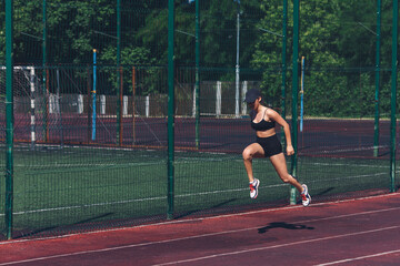 the girl makes jumps to warm up. Playing sports on the sports ground.