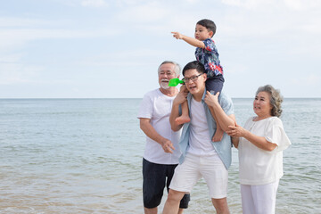 Asian family walking on the beach together. son sitting on father's shoulder with support from...