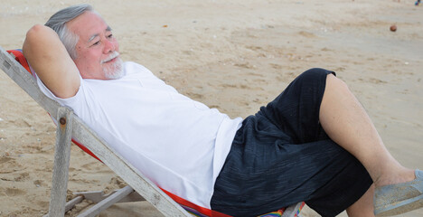 Asian senior man sitting on beach chair relax and enjoy of beach environment on holiday trip....