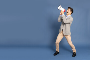 Young Asian business man holding megaphone isolated on blue background, Speaker and announce...