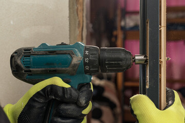 Drilling a hole in the door with a green screwdriver, close-up of the drilling process,