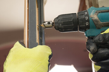 Drilling a hole in the door with a green screwdriver, close-up of the drilling process,