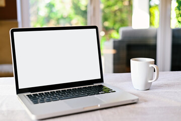 Fototapeta premium Front view of white screen laptop in the living room near to the garden. Remote work. freelance.Work from home. Telework