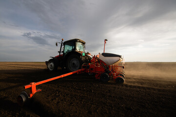 Farmer with tractor seeding - sowing crops at agricultural field