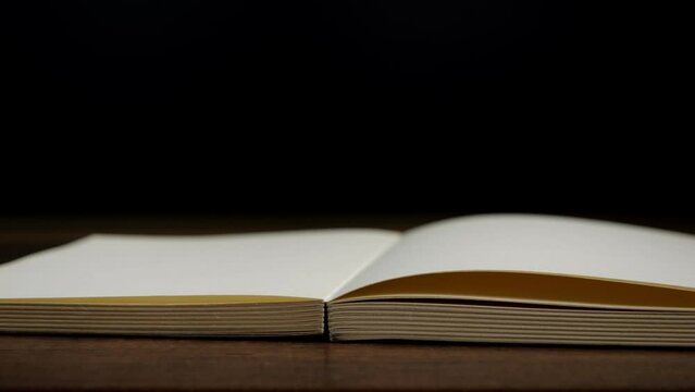 4K-Slow motion of open book with blank page fallowing on wooden table with black background, Education and business concept.