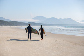 surfer couple walking on the beach