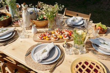 Served table with homemade food, drinks, glasses, plates, wildflowers and other stuff prepared for outdoor party on the countryside