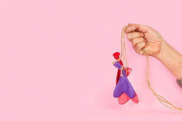 Mano de mujer sosteniendo globos en forma de corazón desinflados sobre un fondo rosa pastel liso y...