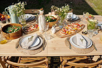 Served wooden table with homemade food, drinks, glasses, plates, wildflowers and other stuff prepared for outdoor party