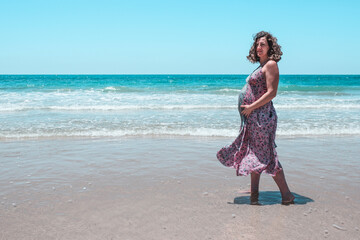 Pregnant woman on the beach. Adult lady on the beach about to give birth. High risk pregnancy. Miss shows the belly of her 8-month-old unborn baby.