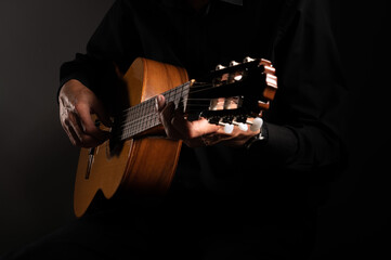 Spanish classical guitar and guitarist's hands up close on a black background with copy space - obrazy, fototapety, plakaty