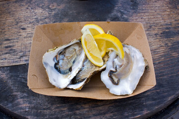 Oysters with lemon in a cardboard dish on a wooden table