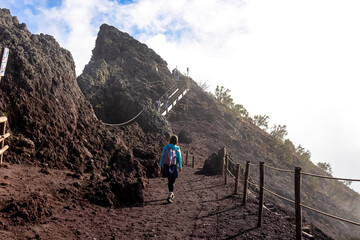 Tourist woman hiking along cloudy edge of active volcano crater of Mount Vesuvius, Province of...