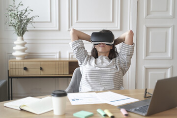 Young glad woman office worker in virtual reality glasses at workplace, relax in VR helmet at work