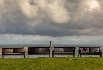Fototapeta premium Four empty, wooden benches looking out to sea by the North Pier of the mouth of the River Tyne on a cloudy day